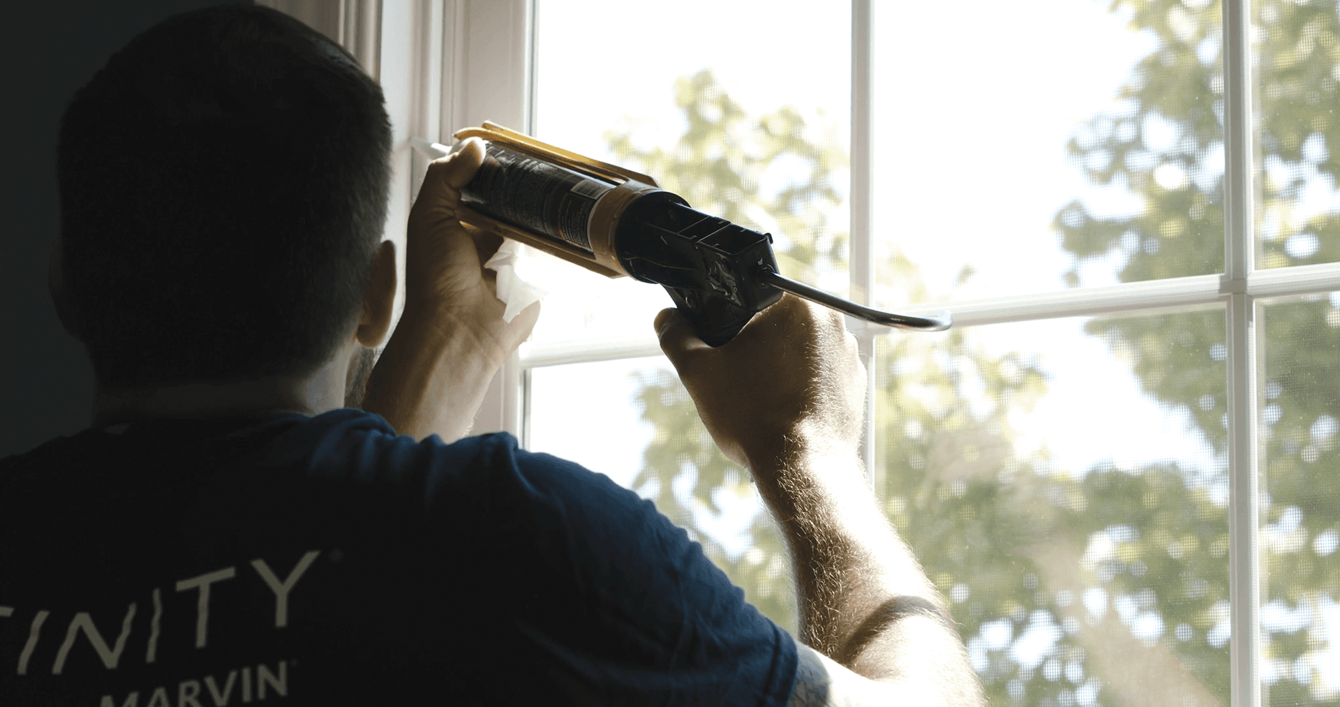 An Infinity from Marvin window installer uses a caulk gun to seal a window.