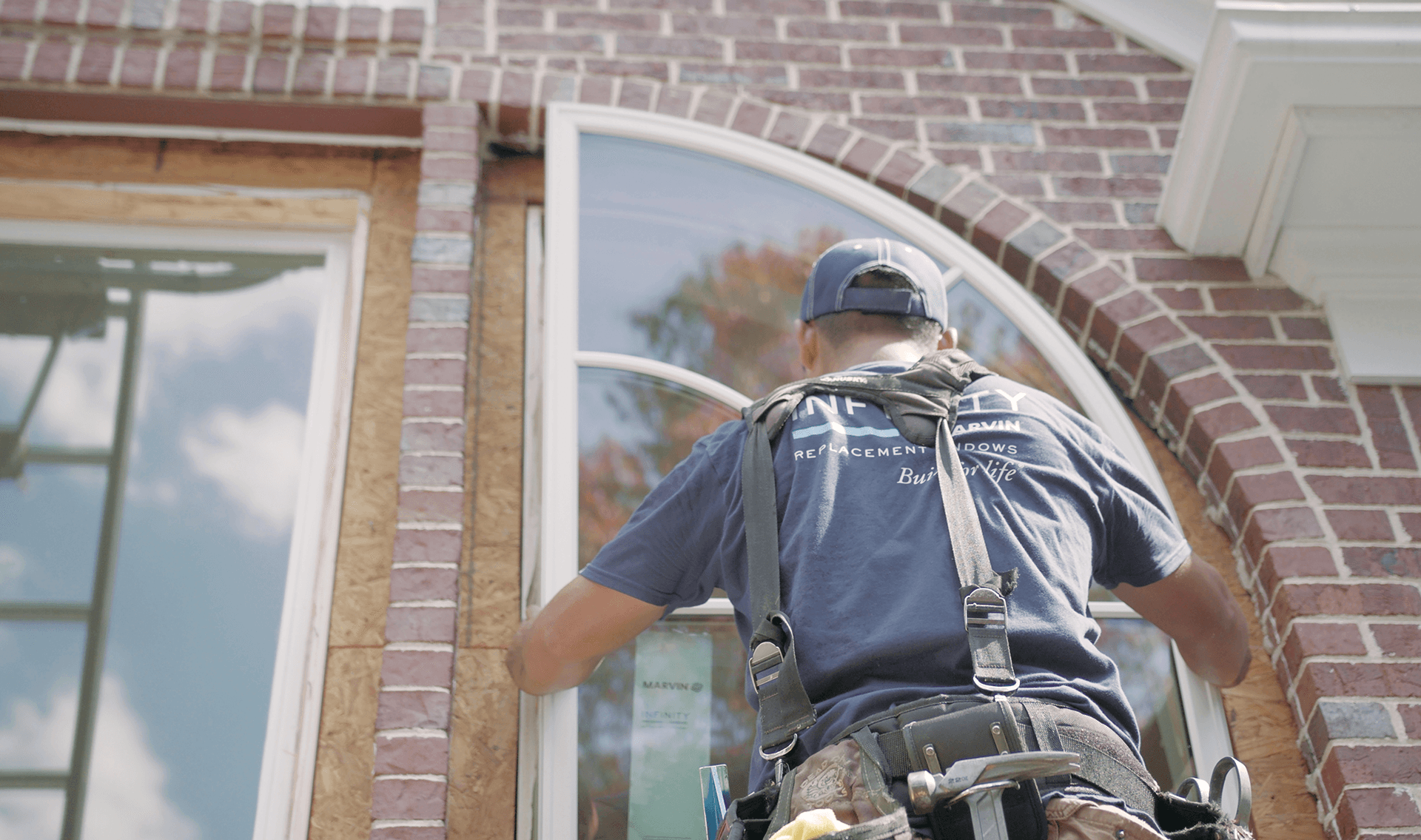 An Infinity windows installer places an arch window in a brick home.