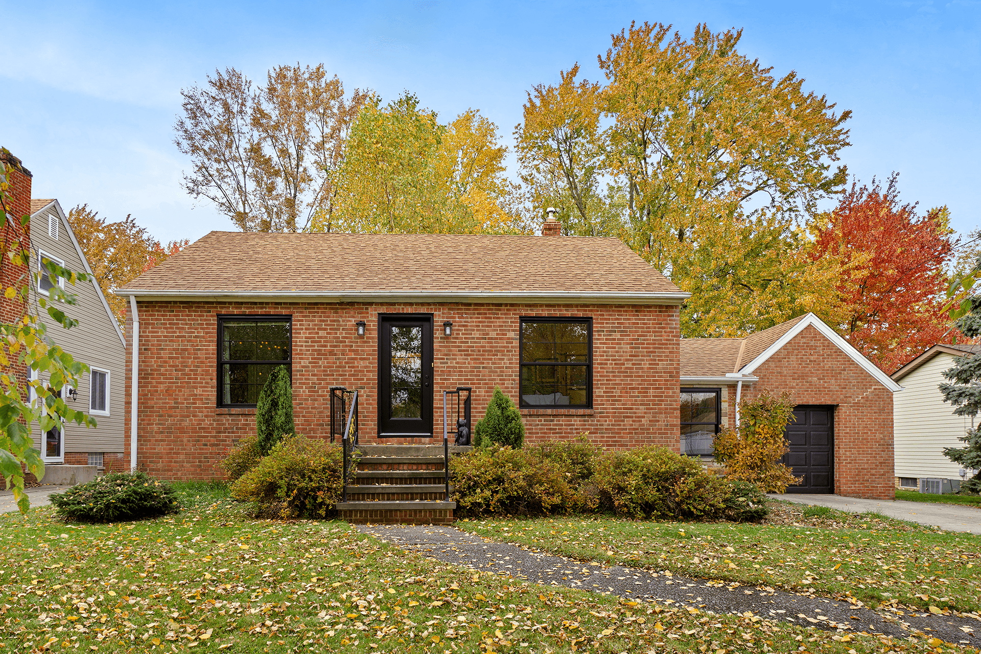 Exterior view of a brick home during fall with black windows and entry door.