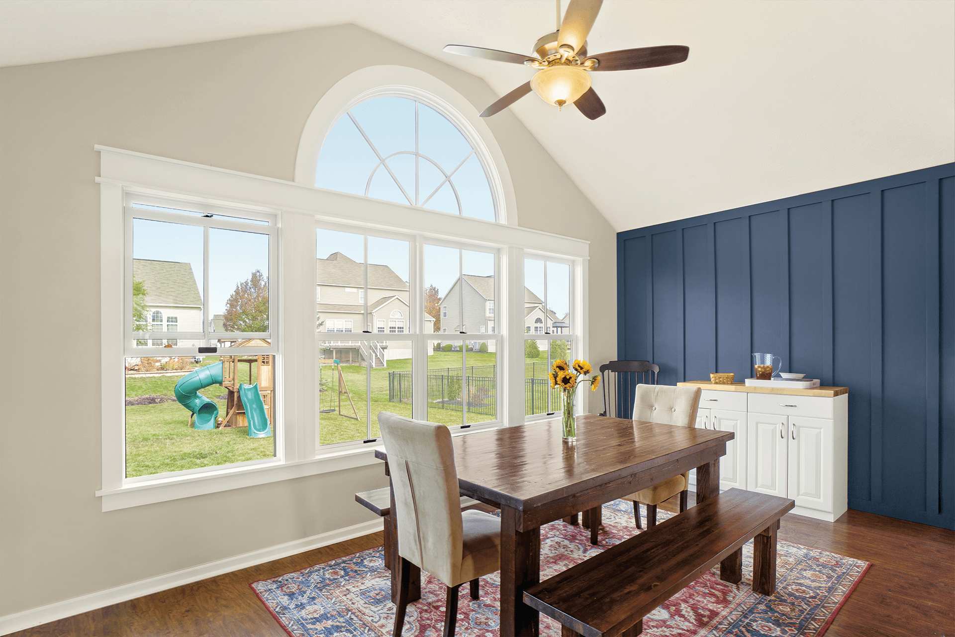 A dining space with a blue wall and white double hung windows with an arch window above.