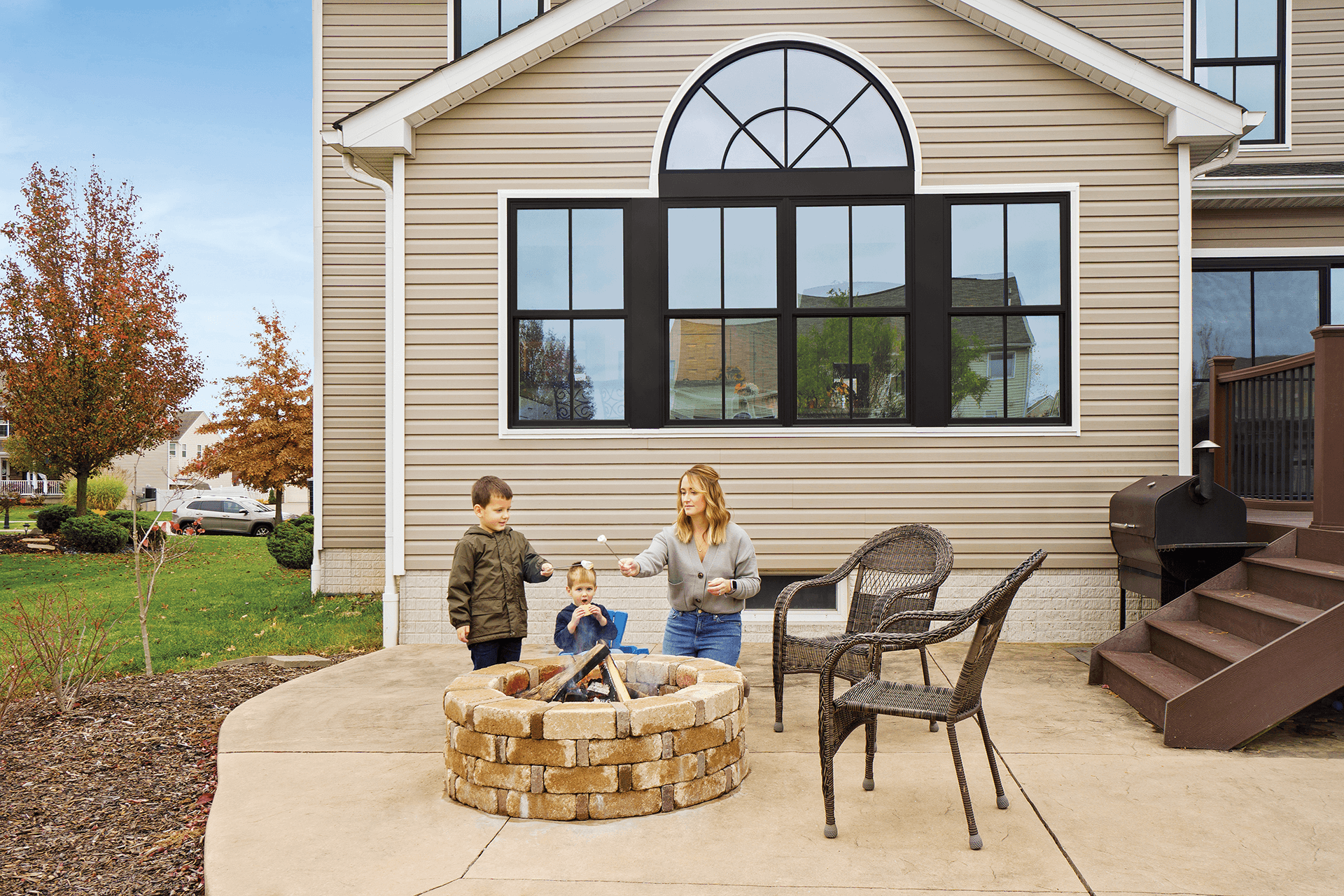 A blonde mother roasts marshmallows with her young sons outside in a round firepit.