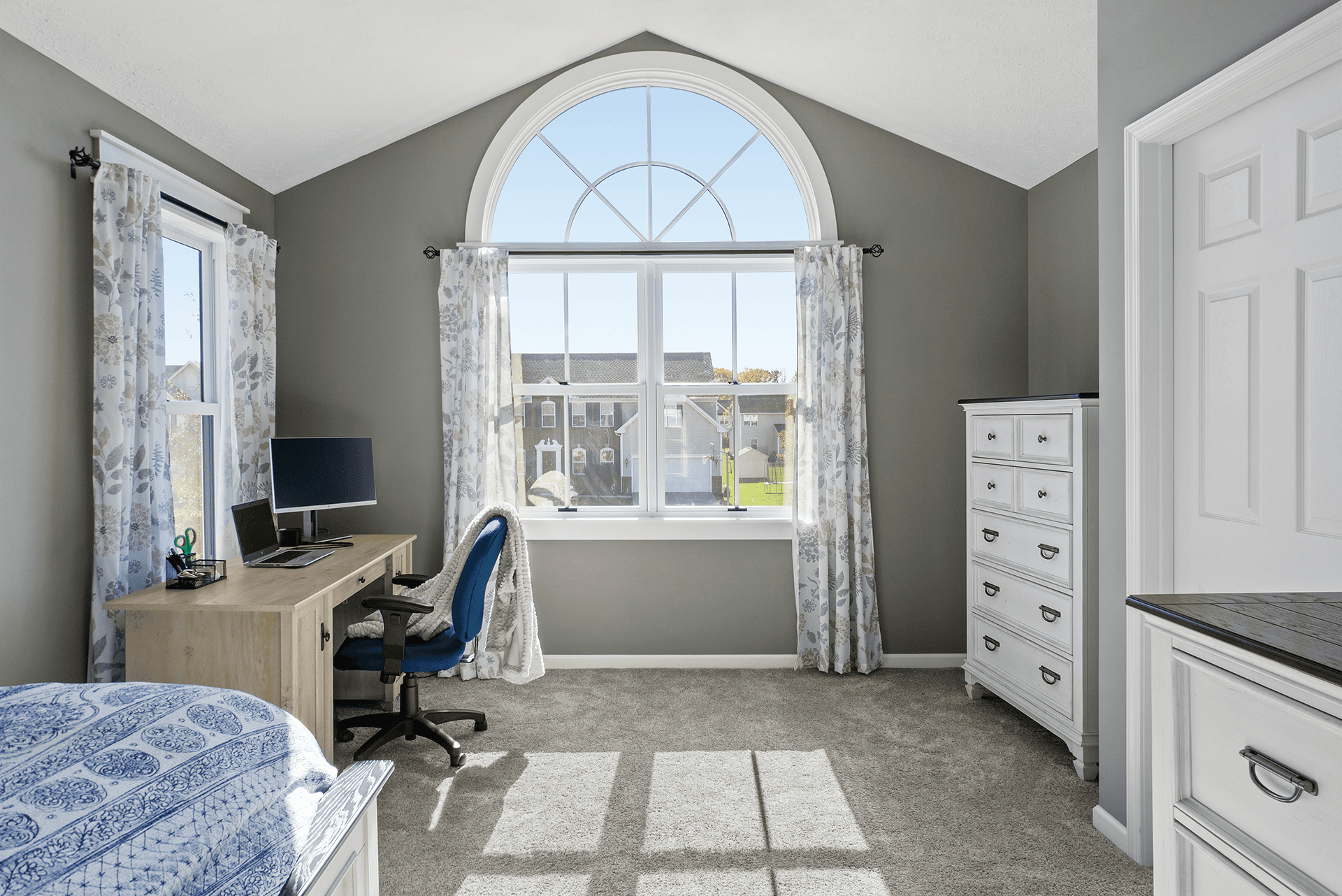 Gray bedroom interior with a large white arch window with divided lites above a pair of double hung windows.