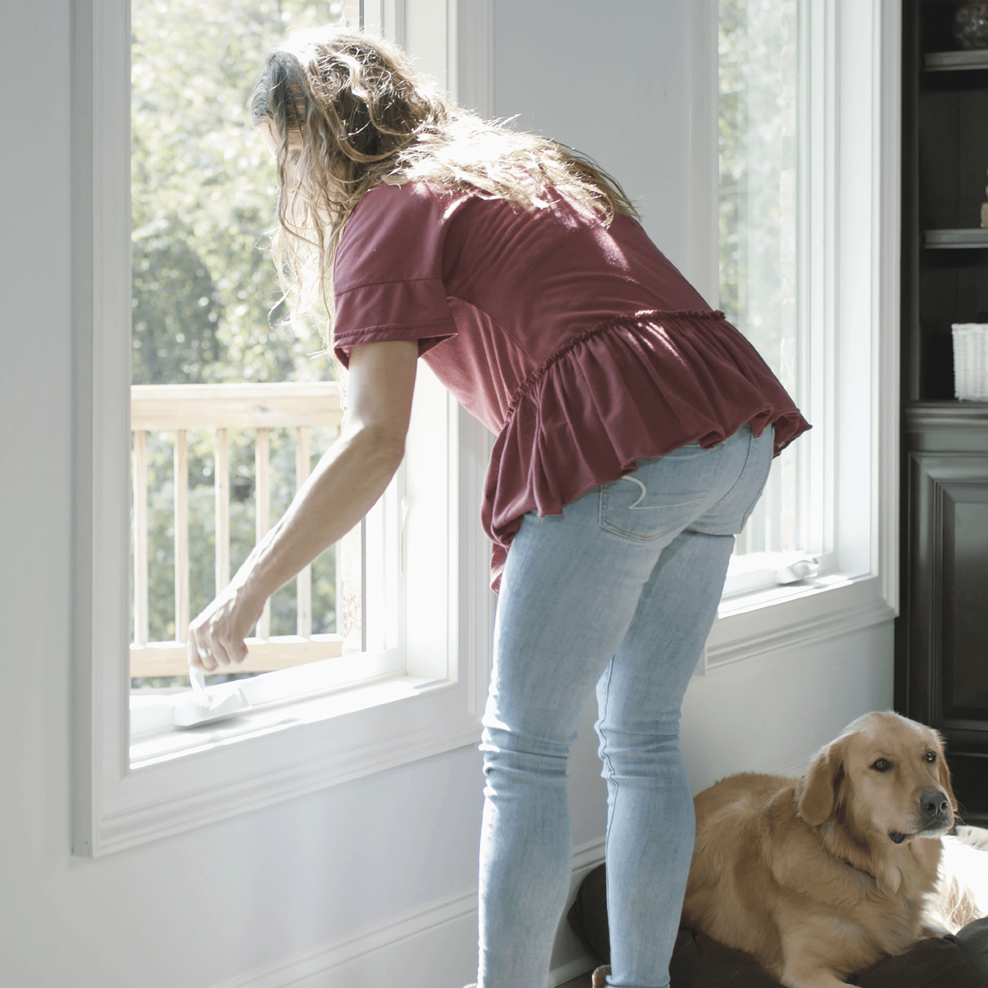 A woman bends down to open a white Infinity casement window.