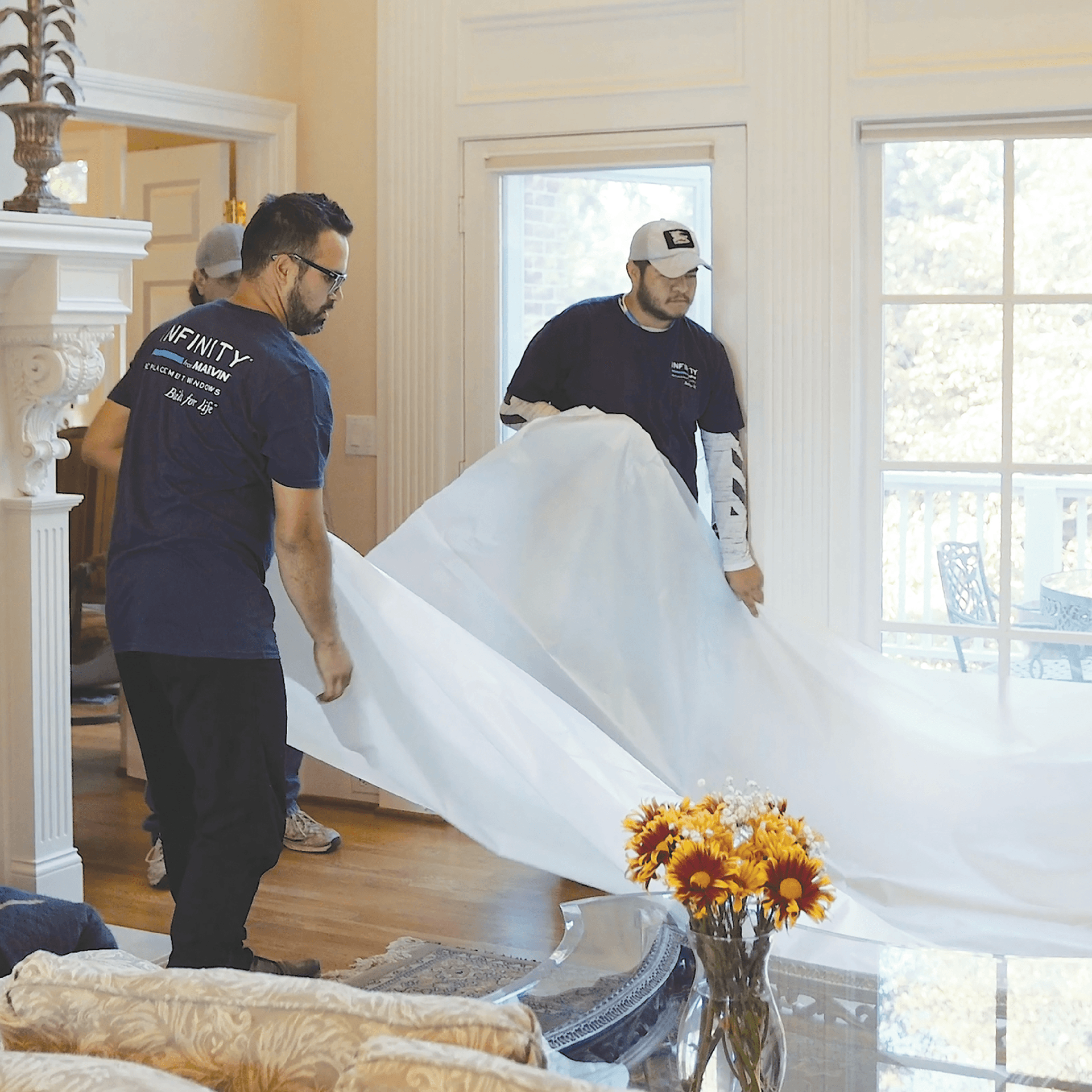 Two Infinity windows installers place a plastic sheet on the floor of an install site.