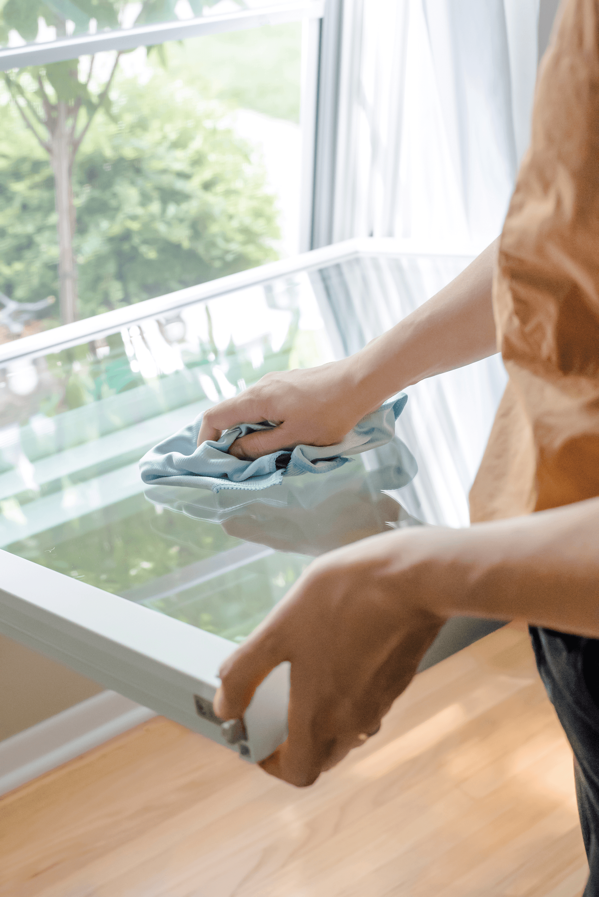 A person uses a blue cloth to clean a tilted-in sash on a double hung window.