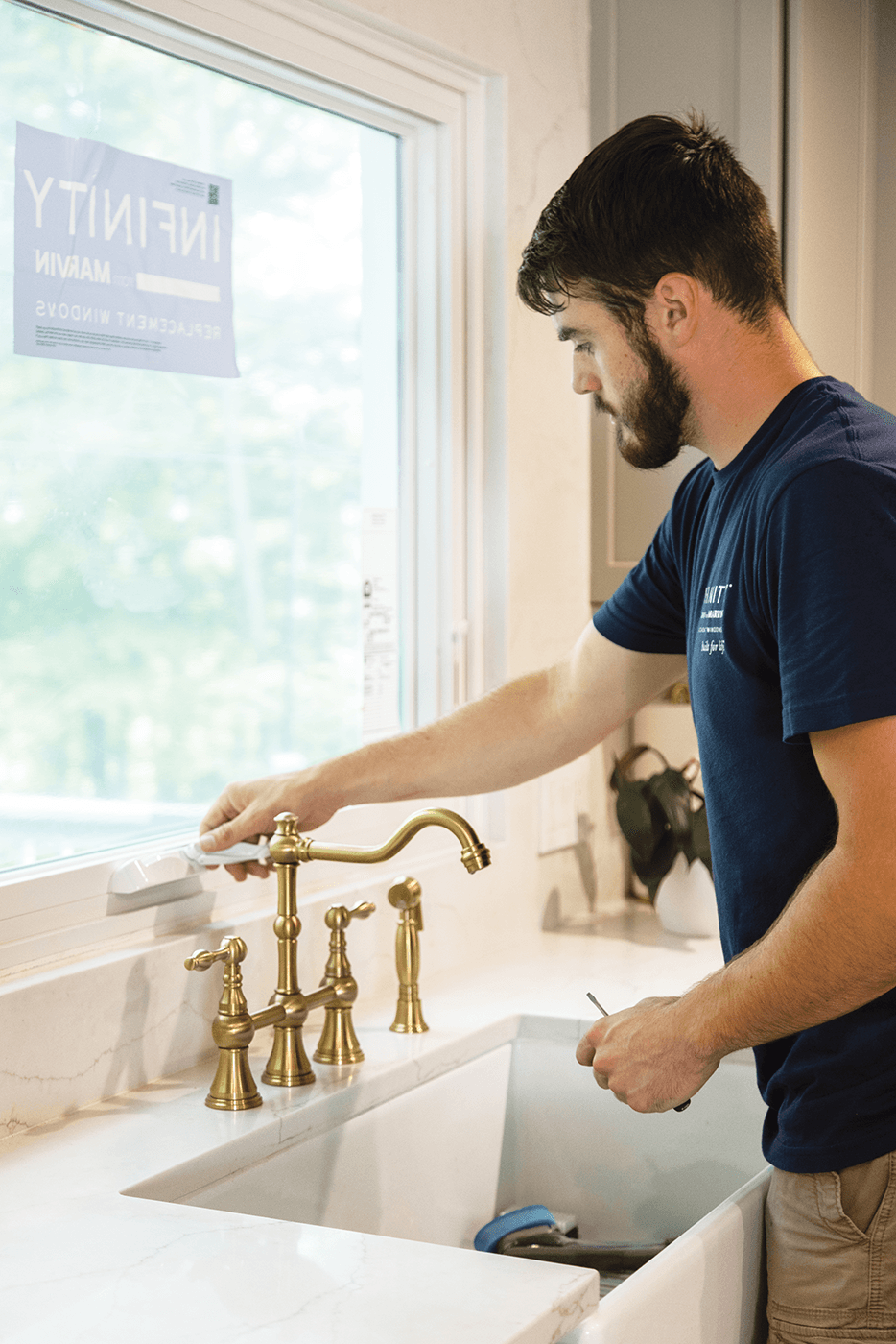 An Infinity window installer tests the handle of a white awning window above a kitchen sink.