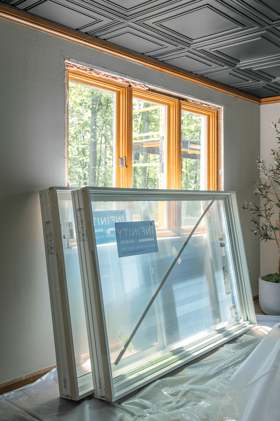 Two large white replacement windows rest against a wall inside a home.